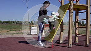 Little beautiful caucasian girl plays in the playground with her mom. Sunny spring weather background, outdoor