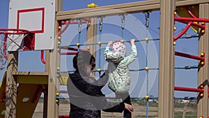 Little beautiful caucasian girl plays in the playground with her mom. Sunny spring weather background, outdoor