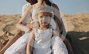 The little beautiful caucasian girl standing between her parents legs. Pregnant mother. Happy family in whote clothes