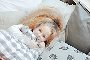 Little beautiful curly blonde girl woke up and smiling, cozy mor