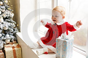 Little beautiful and cute girl dressed as Santa Claus sitting on windowsill and rejoicing