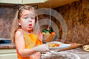 Little beautiful cute girl in orange apron smiling and making homemade pizza, roll the dough at home kitchen. Concept happy family