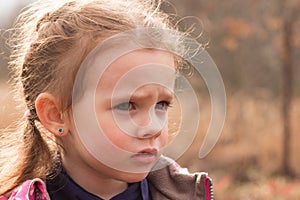 Little beautiful cute sad girl in a jacket with blond hair in pigtails stands on an autumn background