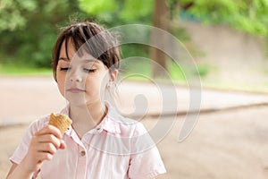 Little beautiful dark-haired girl in a dress eats an ice cream cone in the park