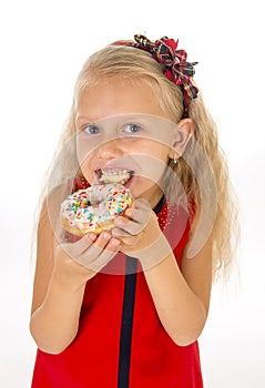 Little beautiful female child with long blonde hair and red dress eating sugar donut with toppings delighted and happy