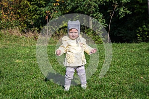 Little beautiful girl baby coat, hat and jeans playing in the park walking on green grass doing their first steps smiling and enjo