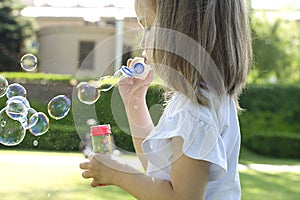 Little beautiful girl blows soap bubbles in the park in summer