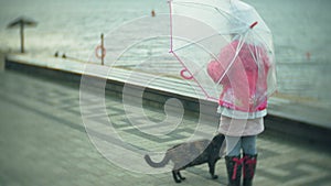 Little beautiful girl and cat with umbrella playing in the rain eating ice cream on the coast