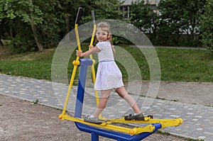 Little beautiful girl child is engaged on simulators on the playground for fitness in the street