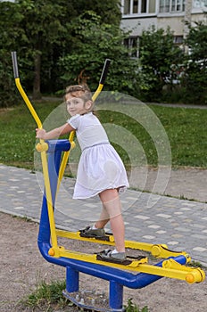 Little beautiful girl child is engaged on simulators on the playground for fitness in the street