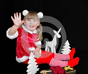 Little beautiful girl in a Christmas Santa suit, with fur balls on her head, holds gifts in her hands and rejoices.