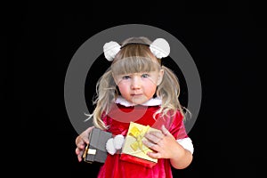 Little beautiful girl in a Christmas Santa suit, with fur balls on her head, holds gifts in her hands and rejoices.