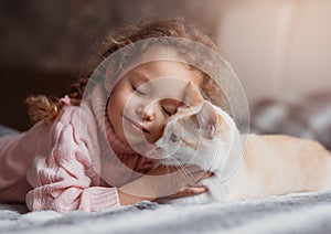 Little beautiful girl cuddles with cat gum on bed photo