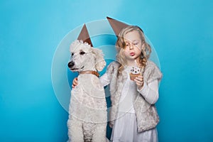 Little beautiful girl with dog celebrate birthday. Friendship. Love. Cake with candle. Studio portrait over blue background