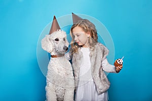 Little beautiful girl with dog celebrate birthday. Friendship. Love. Cake with candle. Studio portrait over blue background