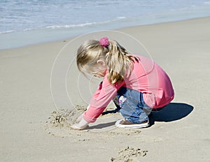 Little beautiful girl draws on sand