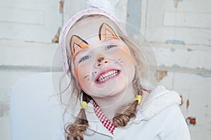 Little beautiful girl with face painting of fox smiles
