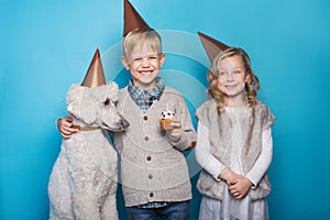 Little beautiful girl and handsome boy with dog celebrate birthday. Friendship. Family. Studio portrait over blue background