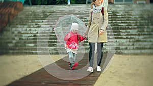 Little beautiful girl and her mother with umbrella playing in the rain