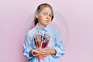 Little beautiful girl holding colored pencils clueless and confused expression