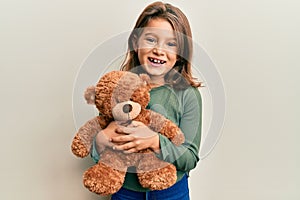 Little beautiful girl hugging teddy bear smiling and laughing hard out loud because funny crazy joke