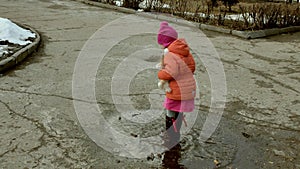 Little beautiful girl jumping on puddles after rain