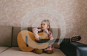 Little beautiful girl learns to play the guitar sitting at home on the couch