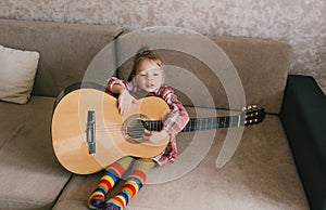 Little beautiful girl learns to play the guitar sitting at home on the couch