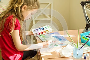 Little beautiful girl painting with watercolors, sitting at home at the table. Child creativity, recreation, development