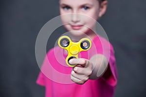 Little beautiful girl in pink t-shirt is playing yellow spinner in hand