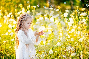 Little beautiful girl playing on the lawn in summer with soap bubbles