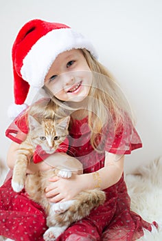 Little Beautiful Girl in Santa Hat Red Party Dress with Little Ginger Kitten Waiting for Christmas and New Year