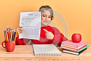 Little beautiful girl showing a passed exam smiling happy pointing with hand and finger