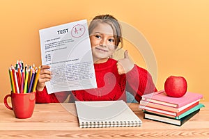 Little beautiful girl showing a passed exam smiling happy and positive, thumb up doing excellent and approval sign