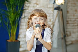 A little beautiful girl sings in a microphone. The concept is ch