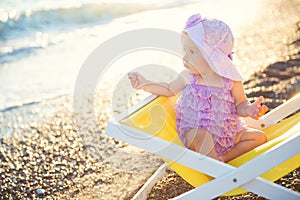 Little beautiful girl sits on a deckchair and throws pebbles into the sea