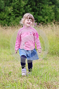 Little beautiful girl in skirt going and hamming at green meadow photo