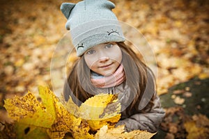 Little beautiful girl stands with a bouquet of maple orange leaves in the autumn park. They are looking at the camera and smiling