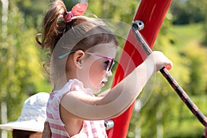 Little beautiful girl in sun-protective glasses with pigtails on the playground