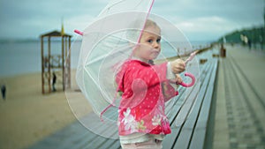 Little beautiful girl with umbrella playing in the rain eating ice cream on the coast