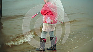 Little beautiful girl with umbrella, playing in the rain, walking along the coast