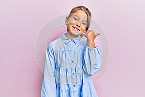 Little beautiful girl wearing casual clothes pointing thumb up to the side smiling happy with open mouth