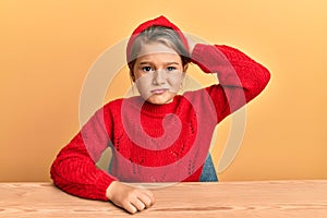 Little beautiful girl wearing casual clothes sitting on the table confuse and wonder about question