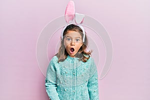 Little beautiful girl wearing cute easter bunny ears afraid and shocked with surprise expression, fear and excited face