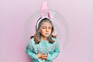 Little beautiful girl wearing cute easter bunny ears with hand on stomach because indigestion, painful illness feeling unwell