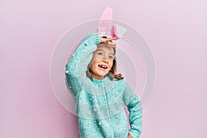 Little beautiful girl wearing cute easter bunny ears very happy and smiling looking far away with hand over head