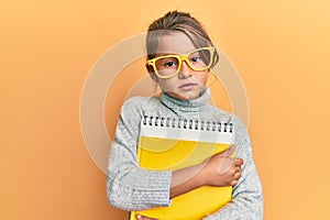 Little beautiful girl wearing glasses and holding books relaxed with serious expression on face