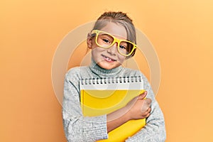 Little beautiful girl wearing glasses and holding books smiling with a happy and cool smile on face