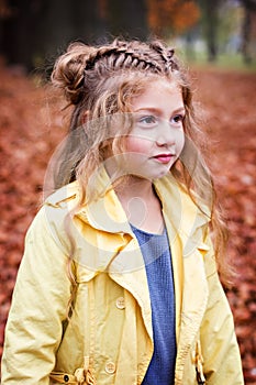 Little beautiful girl in a yellow raincoat walks in the park