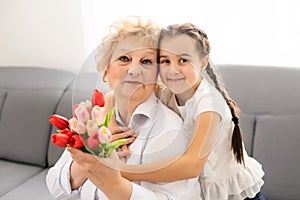 Little beautiful granddaughter gives her grandmother a bouquet of pink tulips. The concept of family, respect